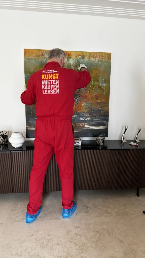 Mitarbeiter von ARTprotect trägt ein Originalgemälde ins Wohnzimmer einer Berliner Wohnung